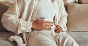 Mujer sentada en el sofá con las manos sobre el vientre por molestias digestivas