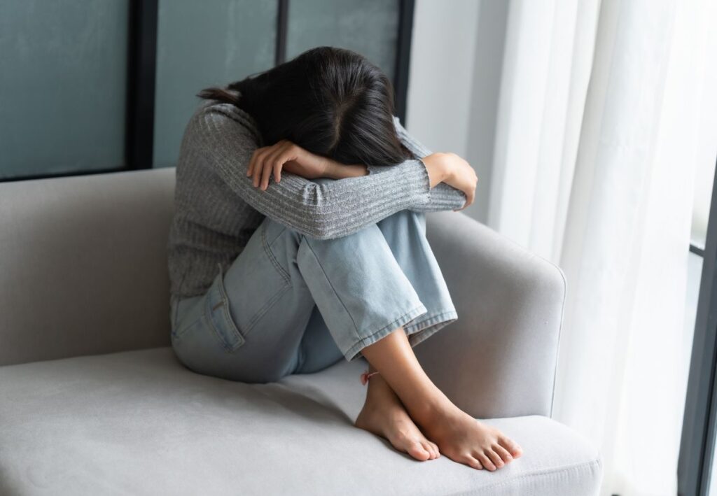 Mujer con estrés y ansiedad sentada en el sofá con la cabeza entre los brazos
