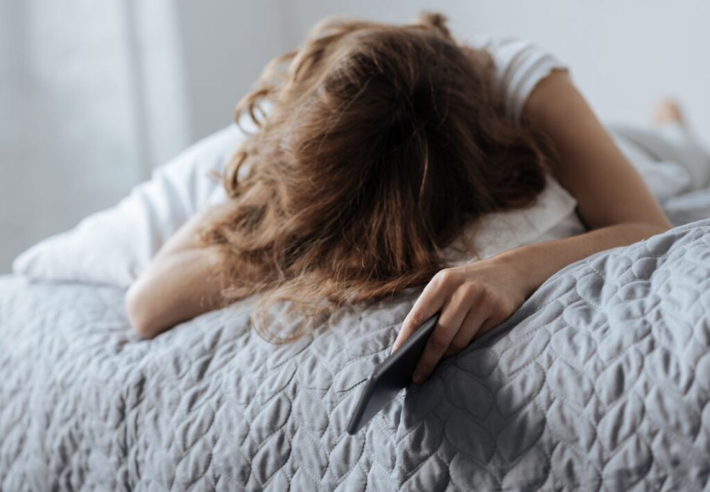 Mujer tumbada en la cama con el móvil, con dificultad para conciliar el sueño