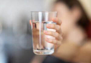 Filename: metales-pesados-agua-contaminacion.jpg Alt: Mujer sosteniendo un vaso de agua, fuente común de exposición a metales pesados