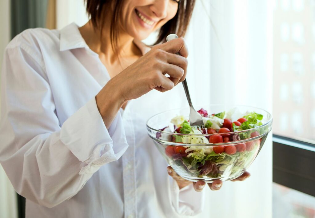 Mujer sonriente comiendo una ensalada fresca de verduras y tomates