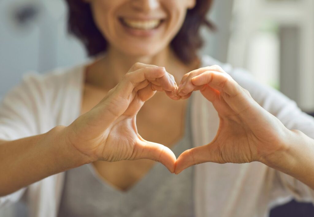 Mujer sonriente formando un corazón con las manos que simboliza el bienestar, la vitalidad y el cuidado cardiovascular asociado a la coenzima Q10