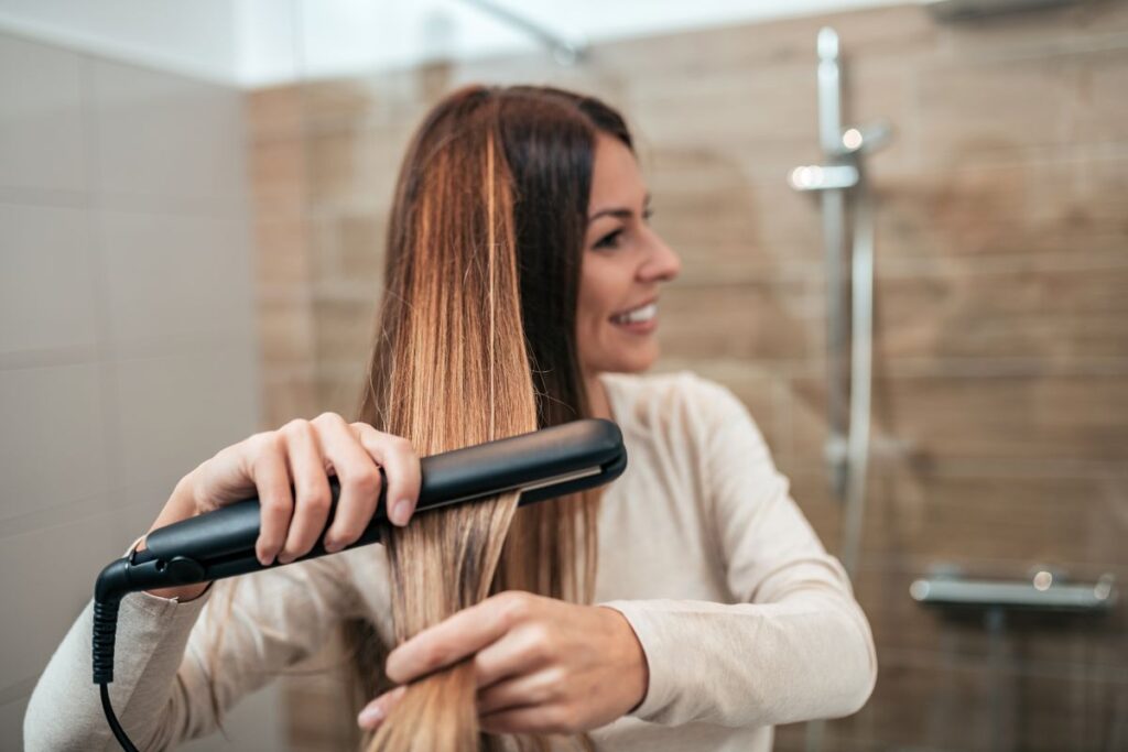 Mujer alisándose el cabello con plancha, un exceso de calor que daña el pelo en verano